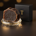 Raw African black soap on a gold-rimmed crystal dish beside a black L'Atelier Trouveur box